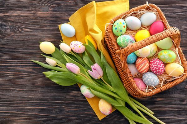 Easter basket with colorful eggs and spring flowers on wooden background, top view